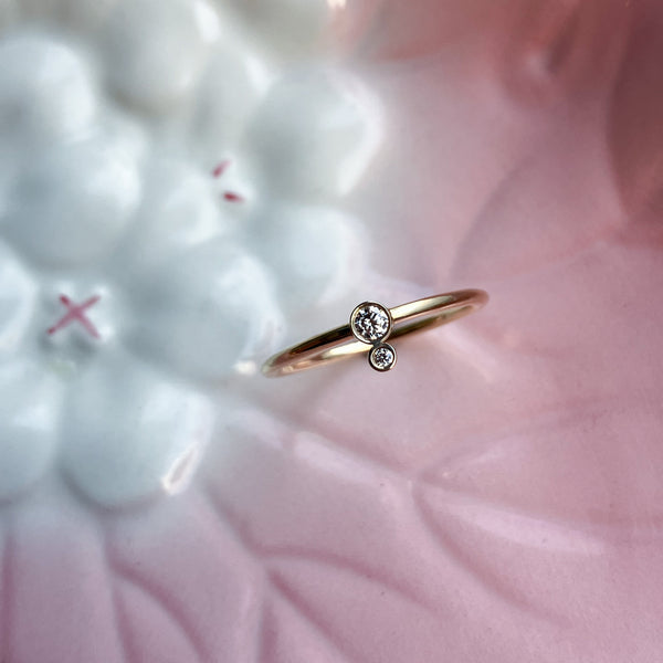 Lækker blank guldring lavet i en blød rundet ringskinne, og to klassiske rørfatninger med champagnefarvede diamanter på i alt 0,06 ct. Den ene fatning sidder i midten af ringskinnen, og den anden sidder på ydersiden, for et klassisk look med et moderne twist