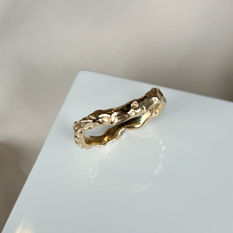 Organisk ring med lækre detaljer i det blankpolerede guld. Ringen har en let kurvet facon, og den organiske overflade gør at lyset blinker smukt i ringen.