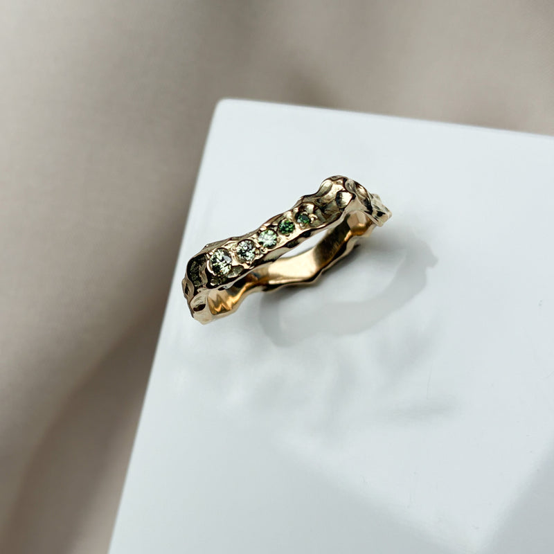 Organisk ring i 14 karat gult guld med kurver og en rå blankpoleret overflade, med smukke grønne diamanter i forskellige nuancer, sat på en række