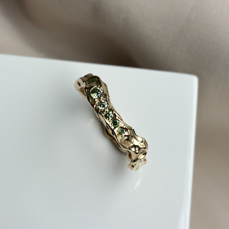 Organisk ring i 14 karat gult guld med kurver og en rå blankpoleret overflade, med smukke grønne diamanter i forskellige nuancer, sat på en række